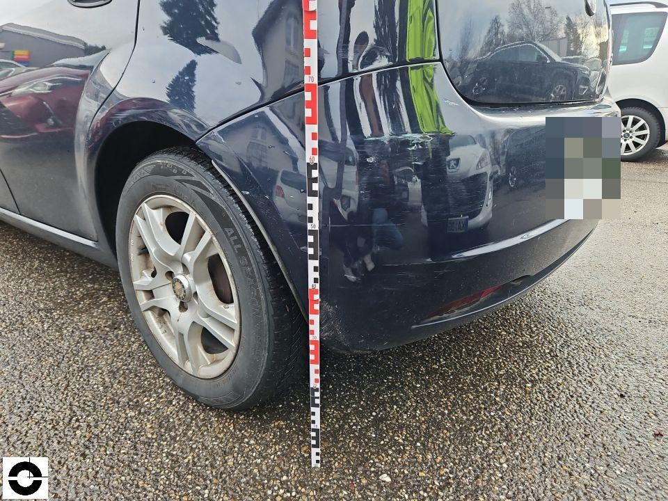 Hintere linke Ecke, Stoßstange mit Kratzern und Schürfspuren, Messlatte zur Dokumentation